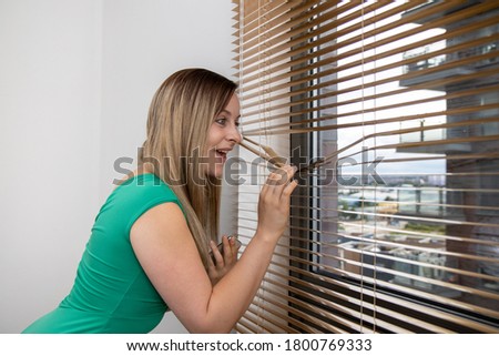 Photo of an attractive woman looking of out of an apartment block window wearing a green dress