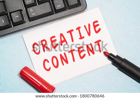 CREATIVE CONTENT text on the business card written in red marker near the keyboard on a blue background