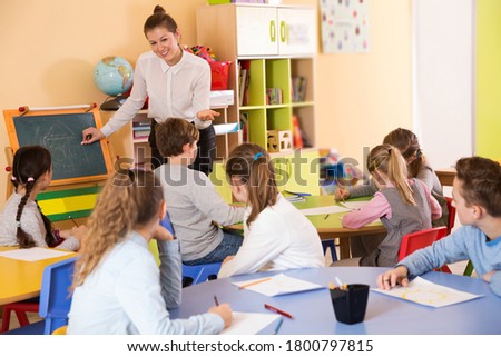 Elementary age group of pupil with glad adult teacher sitting at table and studying