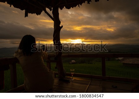 Silhouette woman taking picture of sunset scape at the wooden cottage. 