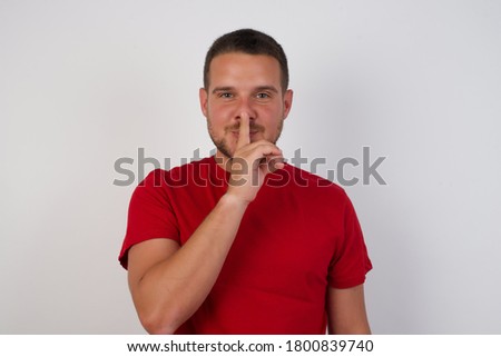 Young handsome man wearing casual red t-shirt over white isolated background asking to be quiet with finger on lips. Silence and secret concept.