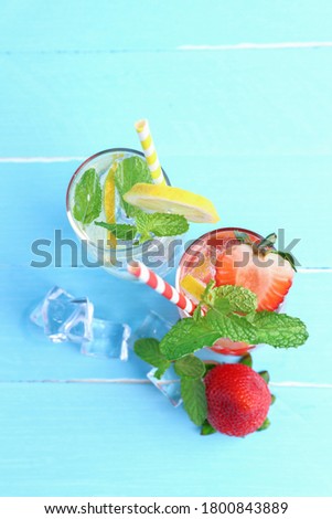 Lemon juice and strawberry juice mixing soda no alcohol in the glass garnish with mint leaves, sliced lime, and half a strawberry on blue wooden table top view with copy space. Concept summer drink.