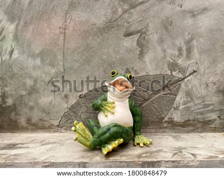 Empty space of wall and Happy singing frog sculpture in front of leaf pattern texture of gray color loft wall for exterior outdoor in the garden