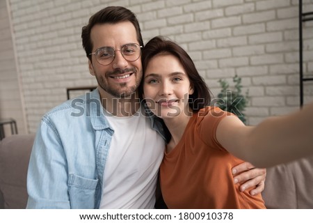 Happy young Caucasian couple hug make self-portrait picture relaxing at home together, smiling man and woman embrace take selfie on smartphone with good quality camera, lover, relations concept