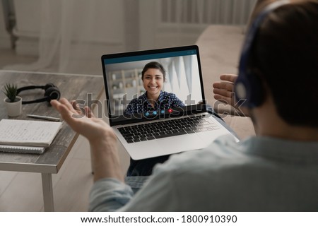 Over shoulder view of man speak talk on video call on laptop with smiling ethnic woman wife, male have webcam virtual digital conference or online business meeting with colleague at home office Royalty-Free Stock Photo #1800910390