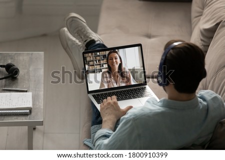 Top back view of man in headphones have webcam digital virtual conference with female colleague or client on laptop, male in earphones speak talk on video call on computer with woman colleague Royalty-Free Stock Photo #1800910399