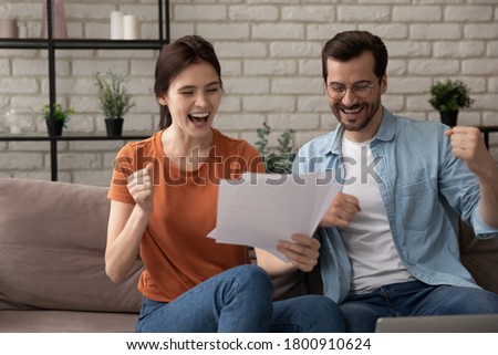 Excited young Caucasian man and woman spouses triumph get good pleasant news in postal letter correspondence, overjoyed millennial couple tenants or renters celebrate bank notice approval Royalty-Free Stock Photo #1800910624