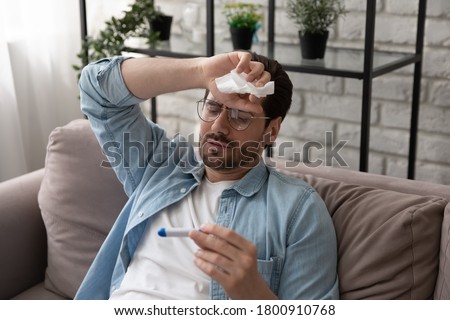 Sick young Caucasian man suffer from fever or flu measure high temperature with thermometer, unhealthy ill male have influenza symptoms, catch cold, struggle with coronavirus, healthcare concept Royalty-Free Stock Photo #1800910768