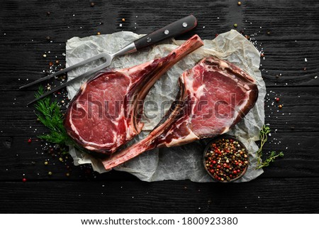 Dry aged raw tomahawk beef steak with spices. On a black wooden background. Top view. Free copy space. Royalty-Free Stock Photo #1800923380