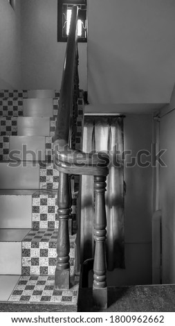 This is a monochrome picture of staircase with black and white checkered tiles and wood railings blur background selective focus on subject