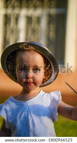 Portrait of funny little girl in white shirt with pan on head