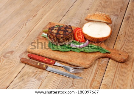 extra thick hot beef meat hamburger lunch on wooden plate with tomatoes and salad over wooden  table with cutlery and fresh sweet bun