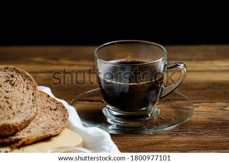 Hot black coffee, americano in glass cup with multi grain chocolate bread on wooden table with black backgraound. Close up.