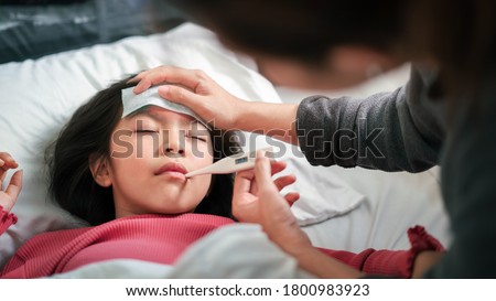 Asian mother measuring temperature girl with digital thermometer in her mouth on bed at morning time, Sick child have cool towel for reduce high fever,  Selective focus, Healthy and infection concept Royalty-Free Stock Photo #1800983923