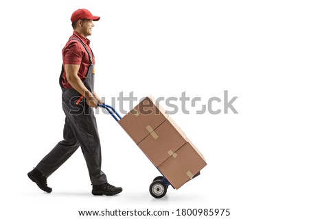 Full length profile shot of a male worker pushing boxes on a hand-truck isolated on white background