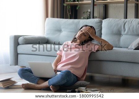 Exhausted millennial female student sit on floor in living room prepare for exam or test suffer from fatigue, tired young ethnic woman study on laptop at home feel overwhelmed, overwork concept Royalty-Free Stock Photo #1800995542