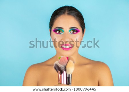 Beauty portrait of female model with vivid makeup and brushes on blue background.