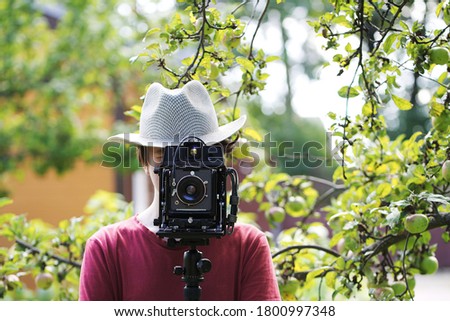 A young man in a hat looks through an old camera on a blurred background of nature.  Soft focus