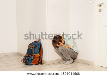 Sad stressed boy bullied in school cry sitting in the corner with son rucksack Royalty-Free Stock Photo #1801011568