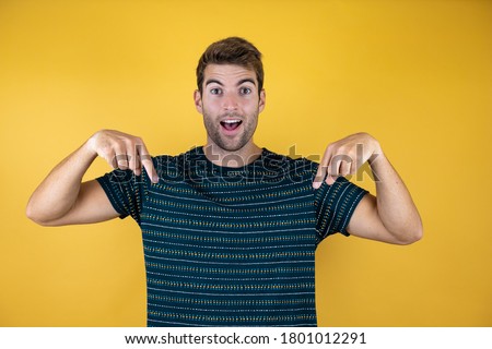 Young handsome man over isolated background amazed smiling with happy face pointing down with two fingers