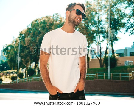 Portrait of handsome smiling stylish hipster lambersexual model.Man dressed in white T-shirt. Fashion male posing on the street background in sunglasses outdoors Royalty-Free Stock Photo #1801027960