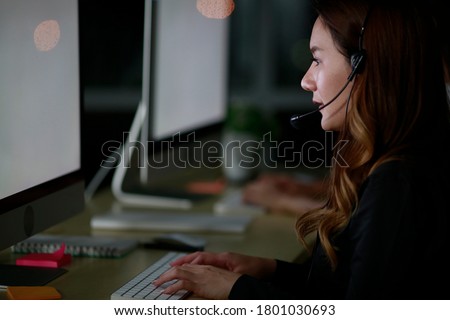 Young Asian lady customer services care operators working night shift in call center for helping assistance client in workplace at night time. Night shift Call center business operator 24hours concept Royalty-Free Stock Photo #1801030693