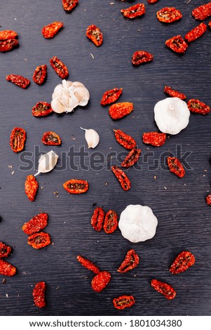 Dried tomatoes, garlic and spices are scattered over a black wooden background. Tomato texture