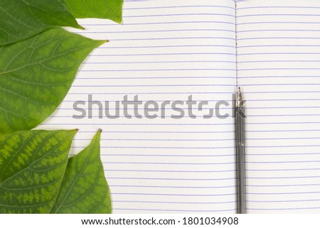 Stationery set. Blank notebook and pen on a background of bright green leaves. Copy space
