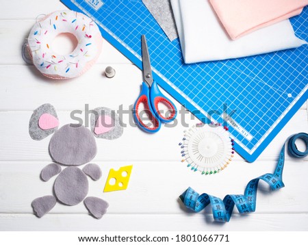 Sewing tools: scissors, several pieces of textile, felt, needles, needle case, cutting mat, tape measure on a white wooden background. Handmade. Toy making. Top view. Copy space.  Royalty-Free Stock Photo #1801066771