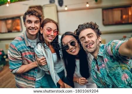 Four friends having fun outdoors. Two young women and two handsome men spending time together near trailer and making selfie. Traveling with motor home.