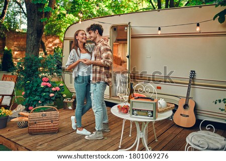 Young couple in love spending time together near trailer. Handsome bearded man and beautiful woman enjoying company of each other, hugging and dancing. Traveling together with motor home.