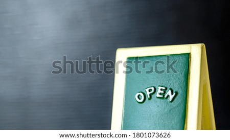 Close up of a green with yellow "OPEN" chalkboard sign leaning against bright with black background.