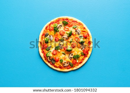 Above view with a whole pizza primavera isolated on a blue colored background. Vegetarian pizza with broccoli, champignons, tomatoes, corn and pepper.