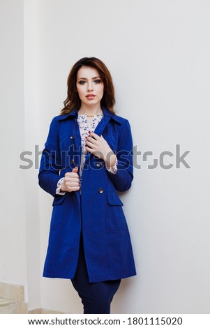 Young woman in retro blazer and  fashionable spring trench coat rest near white wall background. Fashion girl in casual clothes close-up. Youth style.
