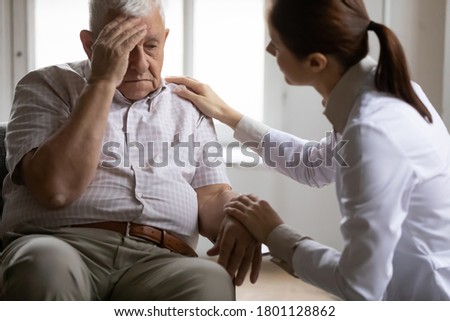 Unhealthy mature old patient complaining to doctor about head ache migraine illness at checkup meeting in clinic. Professional young female general practitioner giving advice, treating elderly man. Royalty-Free Stock Photo #1801128862