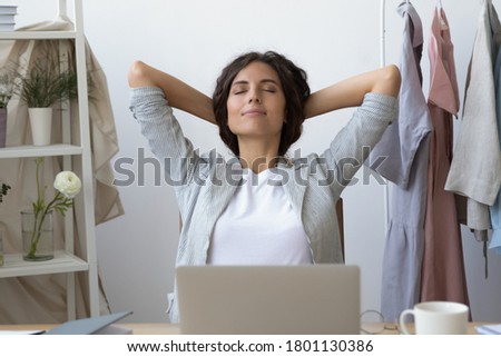 Front view relaxed young businesswoman stretching back, napping with folded hands and closed eyes in modern showroom interior. Happy mindful female creative designer enjoying break moment in atelier. Royalty-Free Stock Photo #1801130386