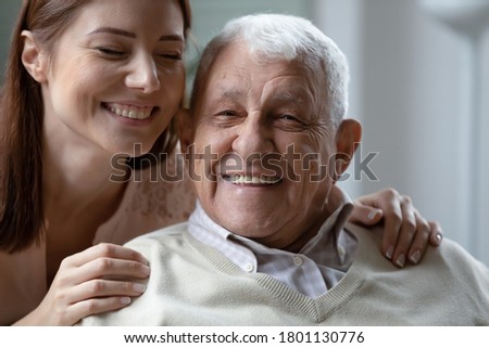 Laughing young woman touching shoulders of happy emotional old mature father, looking at camera. Joyful different generations family enjoying spending fun weekend time together in living room. Royalty-Free Stock Photo #1801130776