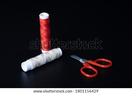 Colored thread for sewing and red color scissors on a black background.