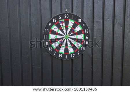 View of dart board with missiles on black wooden wall isolated. Sport and hobby concept.