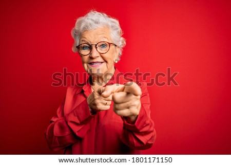 Senior beautiful grey-haired woman wearing casual shirt and glasses over red background pointing fingers to camera with happy and funny face. Good energy and vibes.