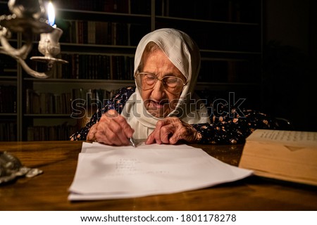 Old lady reading books in dark room with candles light and writing down some notes