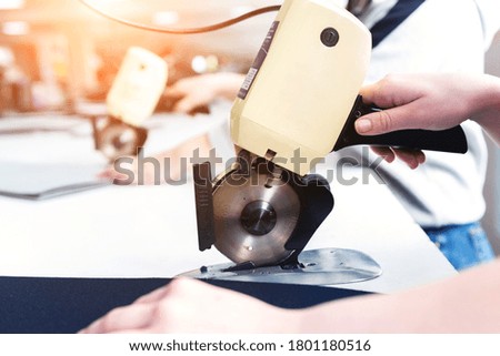 Female worker uses electric cutting fabric machine.