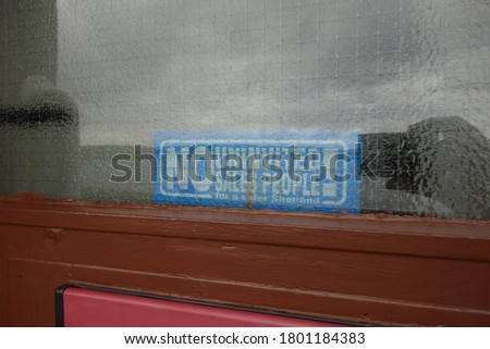 Funny sign "no uninvited sales people for a safer shetland!" behind a glassed door . blue sign with white text . abandoned sales man info sign . Verkaufstyp .