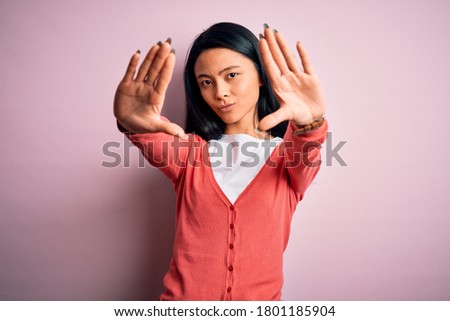 Young beautiful chinese woman wearing casual sweater over isolated pink background doing frame using hands palms and fingers, camera perspective