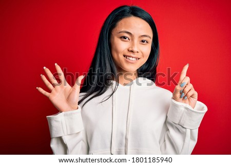 Young beautiful chinese sporty woman wearing sweatshirt over isolated red background showing and pointing up with fingers number six while smiling confident and happy.