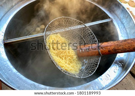 Cooking person in the restaurant is cooking while using a sieve for scalding yellow noodles in a silver pot.Sieve boiled noodles yellow.