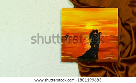 Canvas painting of a romantic couple at sea beach at sunset kept on a golden satin cloth and white textured background 
