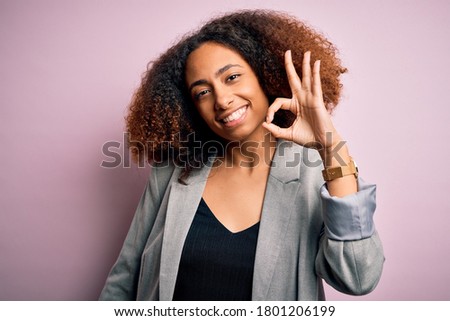 Young african american businesswoman with afro hair wearing elegant jacket smiling positive doing ok sign with hand and fingers. Successful expression.