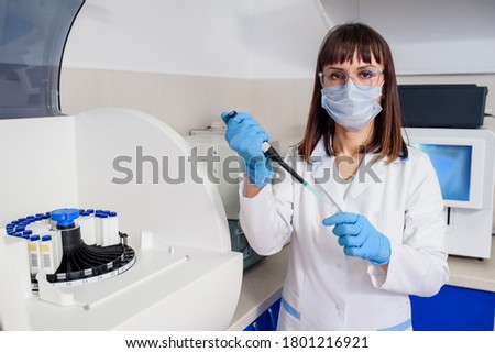 Young woman doctor laboratory assistant is using a micropipette test tubes near a fully-automated diagnostic chemistry system for immunological tests. The hospital laboratories research process. Royalty-Free Stock Photo #1801216921