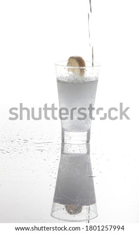 Refreshing sparkling water in a glass with a lemon wedge on white background and water drops around
